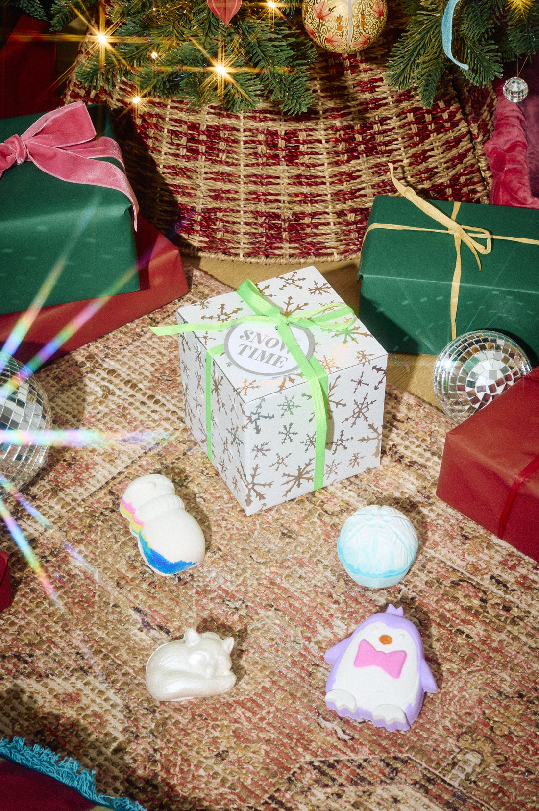 Snow Time gift box surrounded by pale blue, white and pink bath products beneath a Christmas tree.