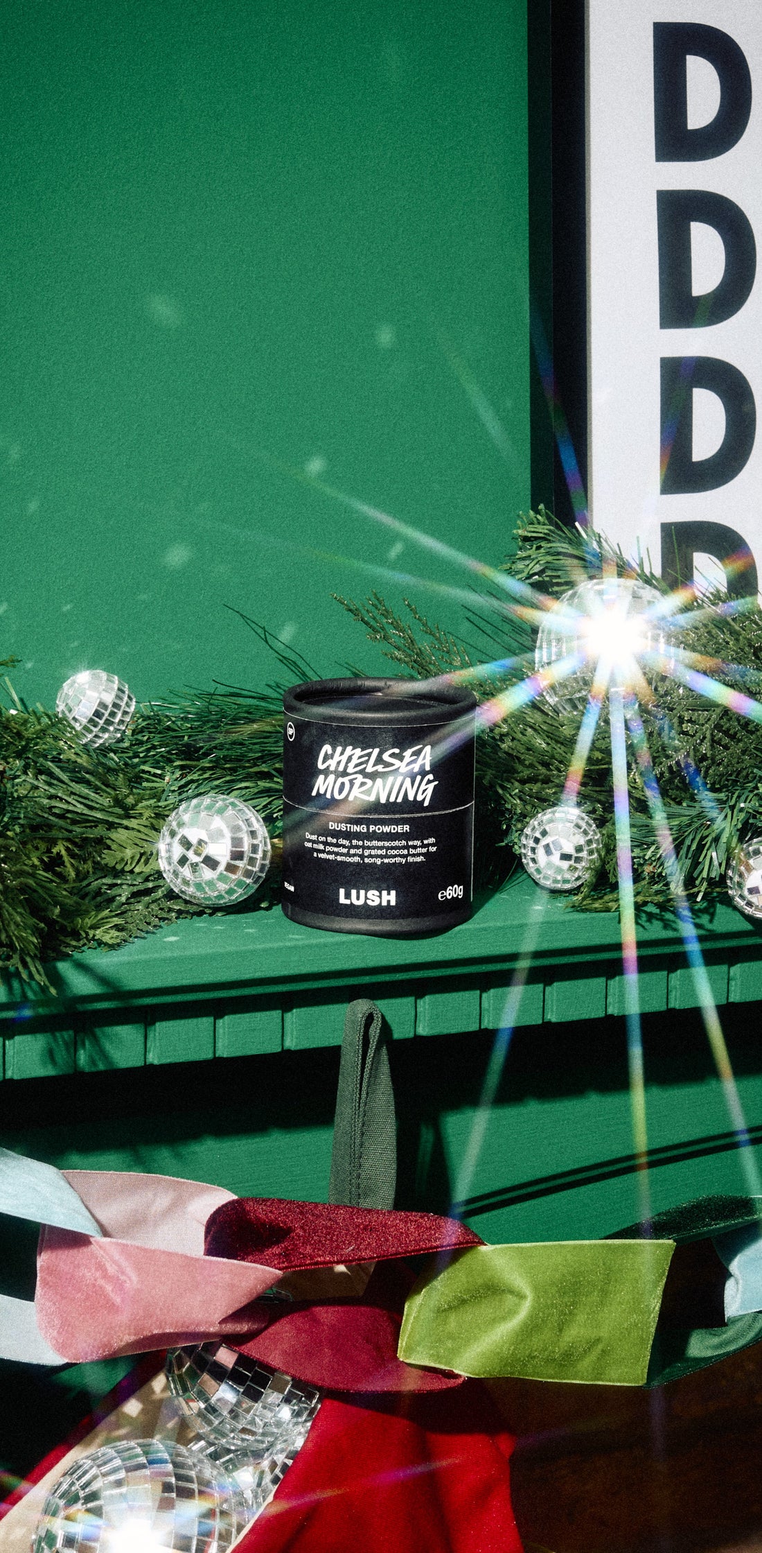 Chelsea Morning dusting powder container among evergreen branches and silver ornaments on a green mantelpiece.