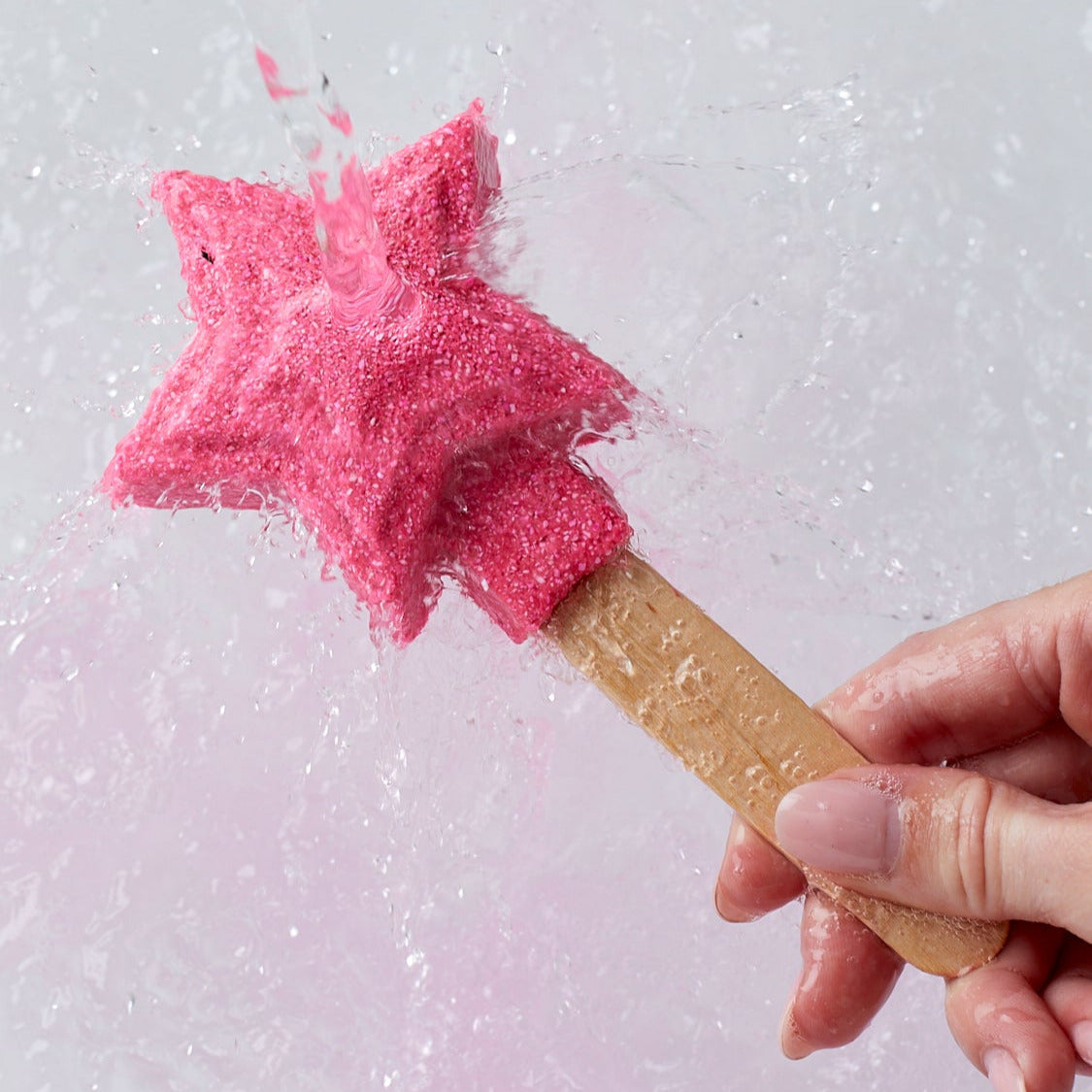 Pink star-shaped candy on a stick held by a hand against a light pink background
