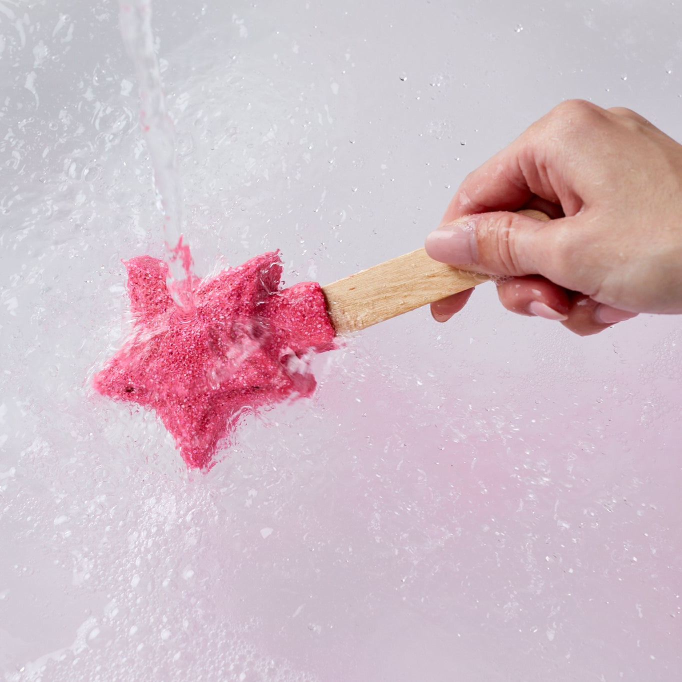 Hand holding a wooden stick with pink star-shaped bubble bar against a light gray background