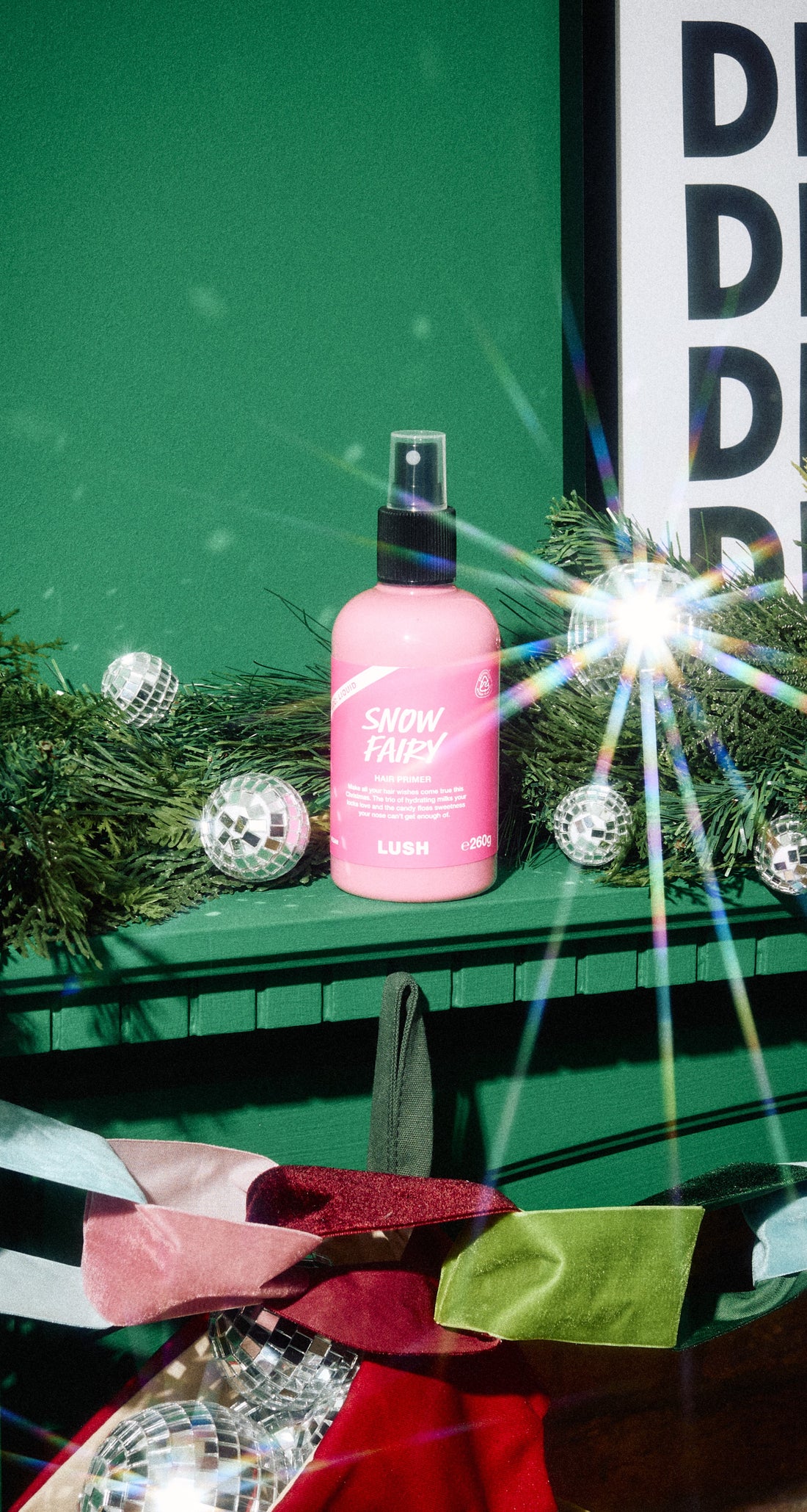 A pink Snow Fairy hair primer bottle displayed on a green mantel among silver baubles and festive foliage.