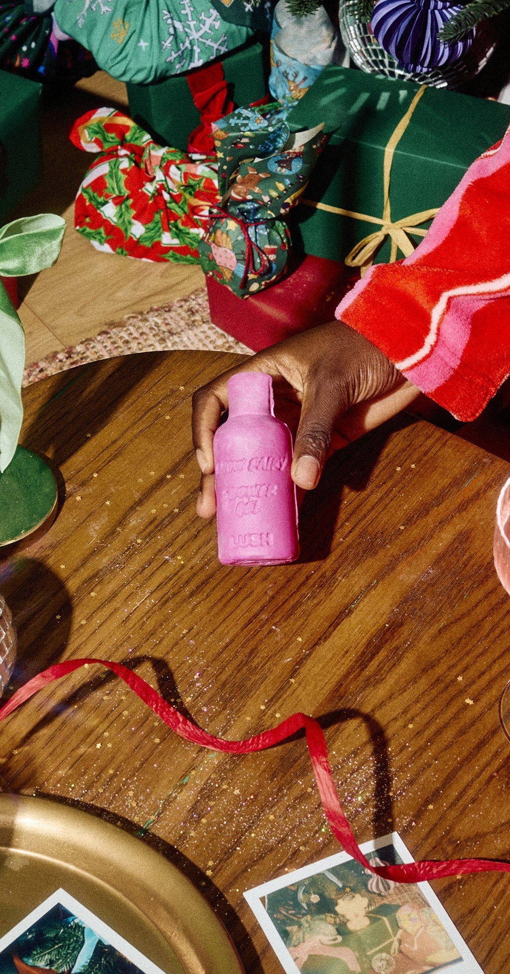 A hand holds pink Snow Fairy naked shower gel on a wooden table among Christmas gifts.