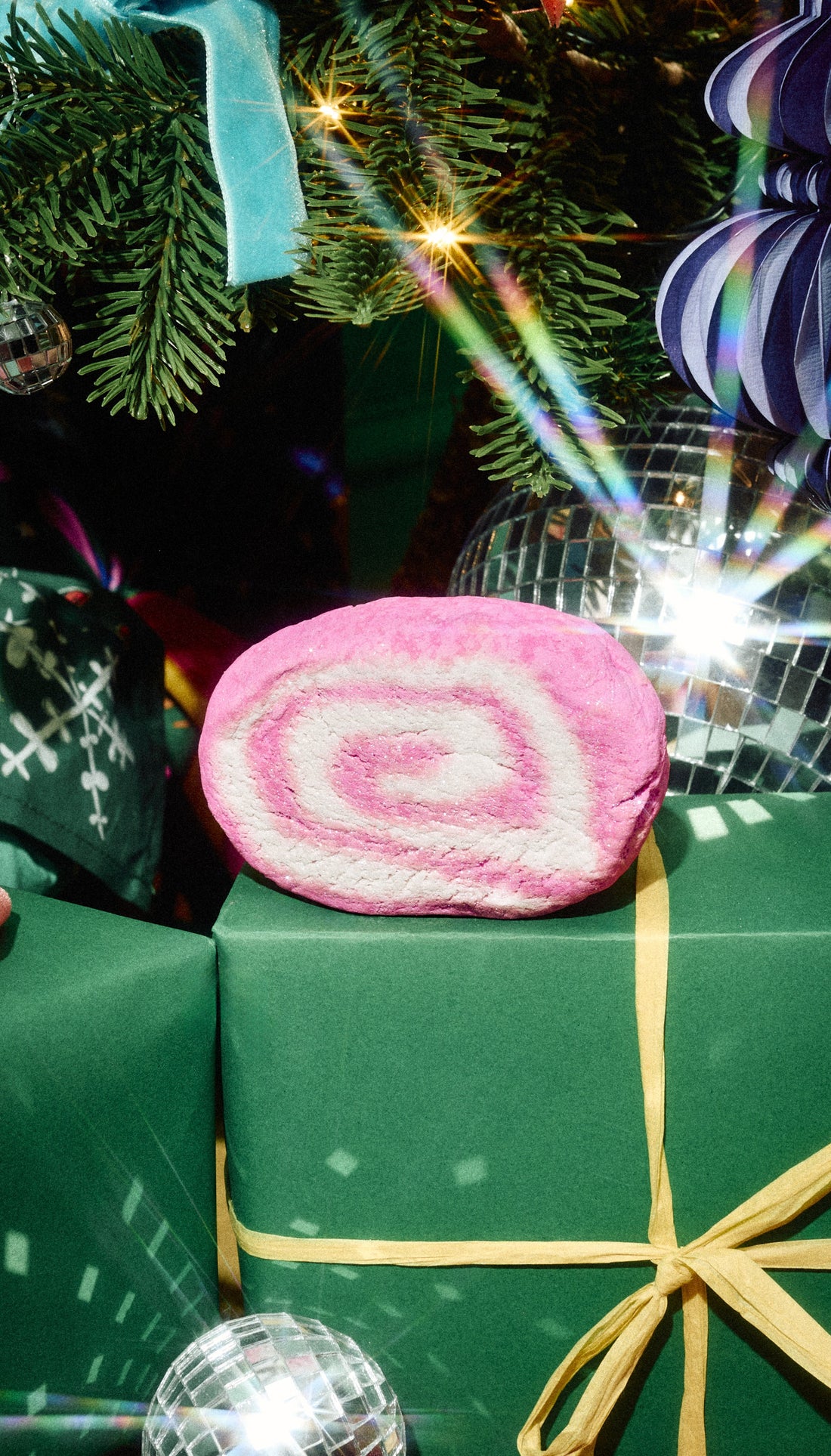 Pink and white spiral Snow Fairy Roll bubble bar displayed on a green present beneath a Christmas tree.