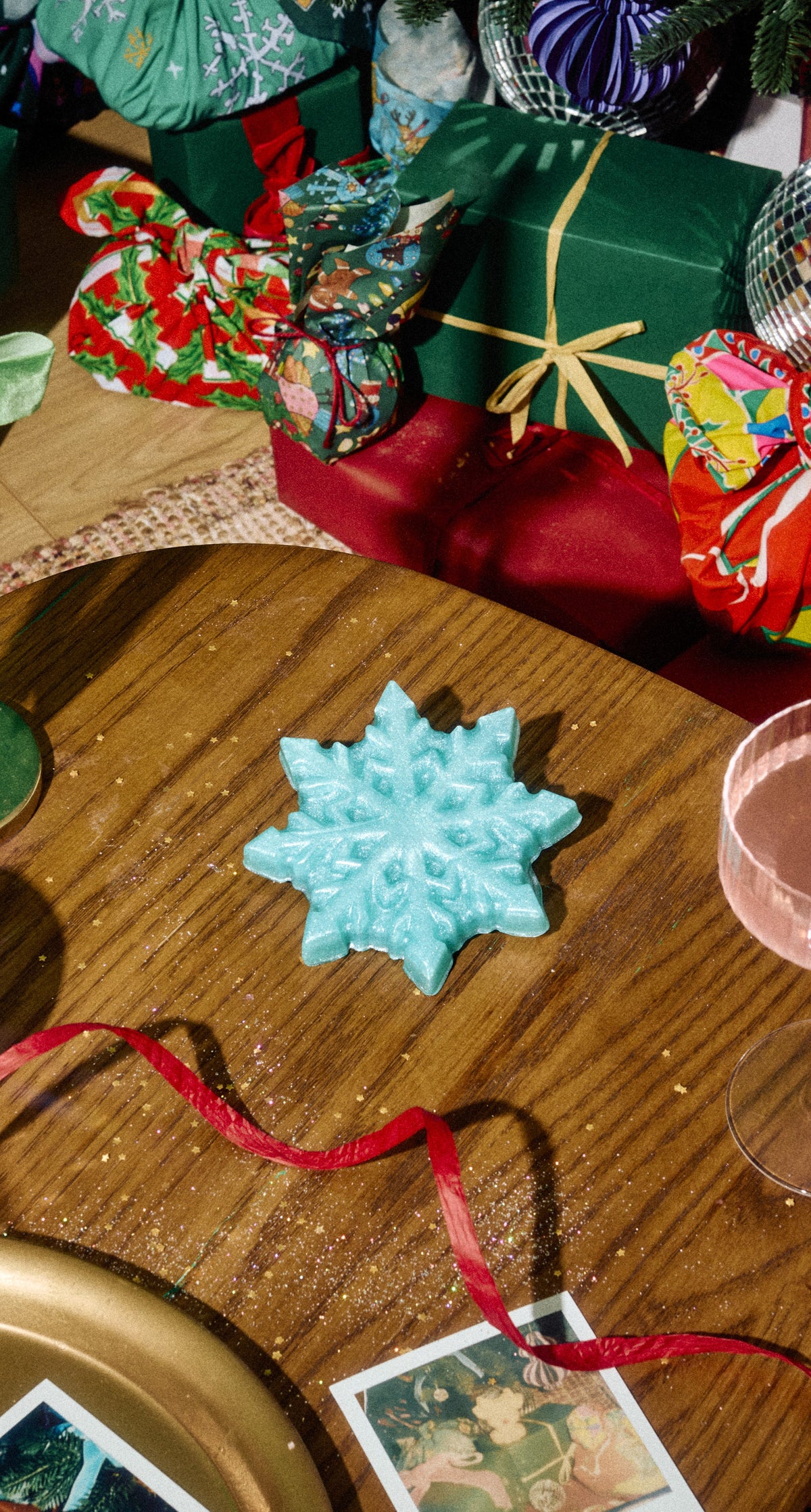 A turquoise snowflake-shaped Snow Flake shower gummy on a wooden table among Christmas gifts.