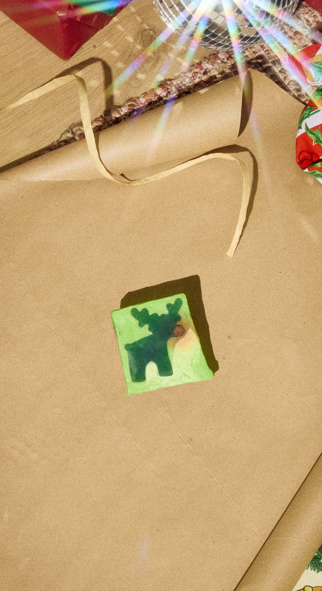 A yellow-green Reindeer soap slice with a dark green reindeer design rests on gold gift wrapping.