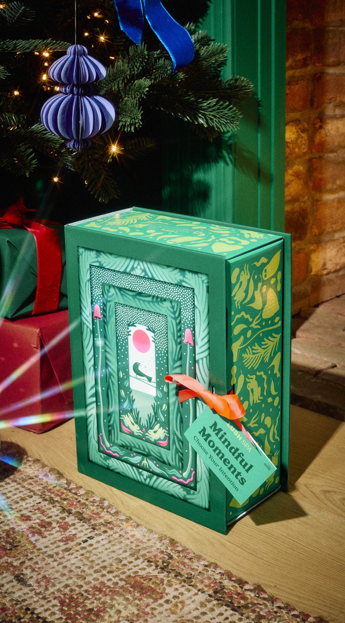Mindful Moments green gift box with an illustrated doorway beneath a Christmas tree.