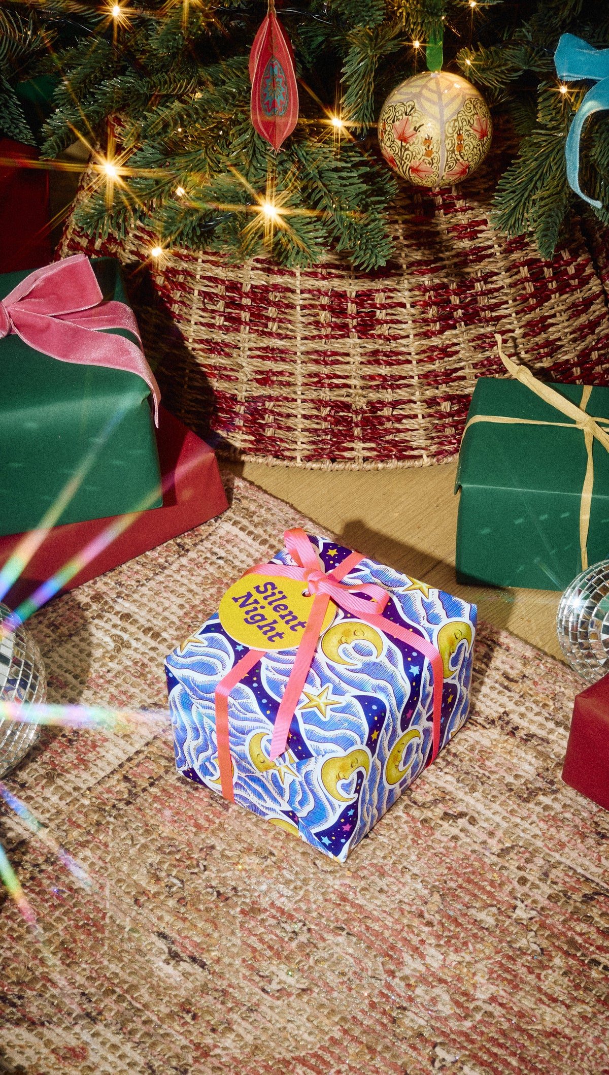 Silent Night gift in blue-and-purple patterned wrapping with a yellow ribbon beside a Christmas tree.