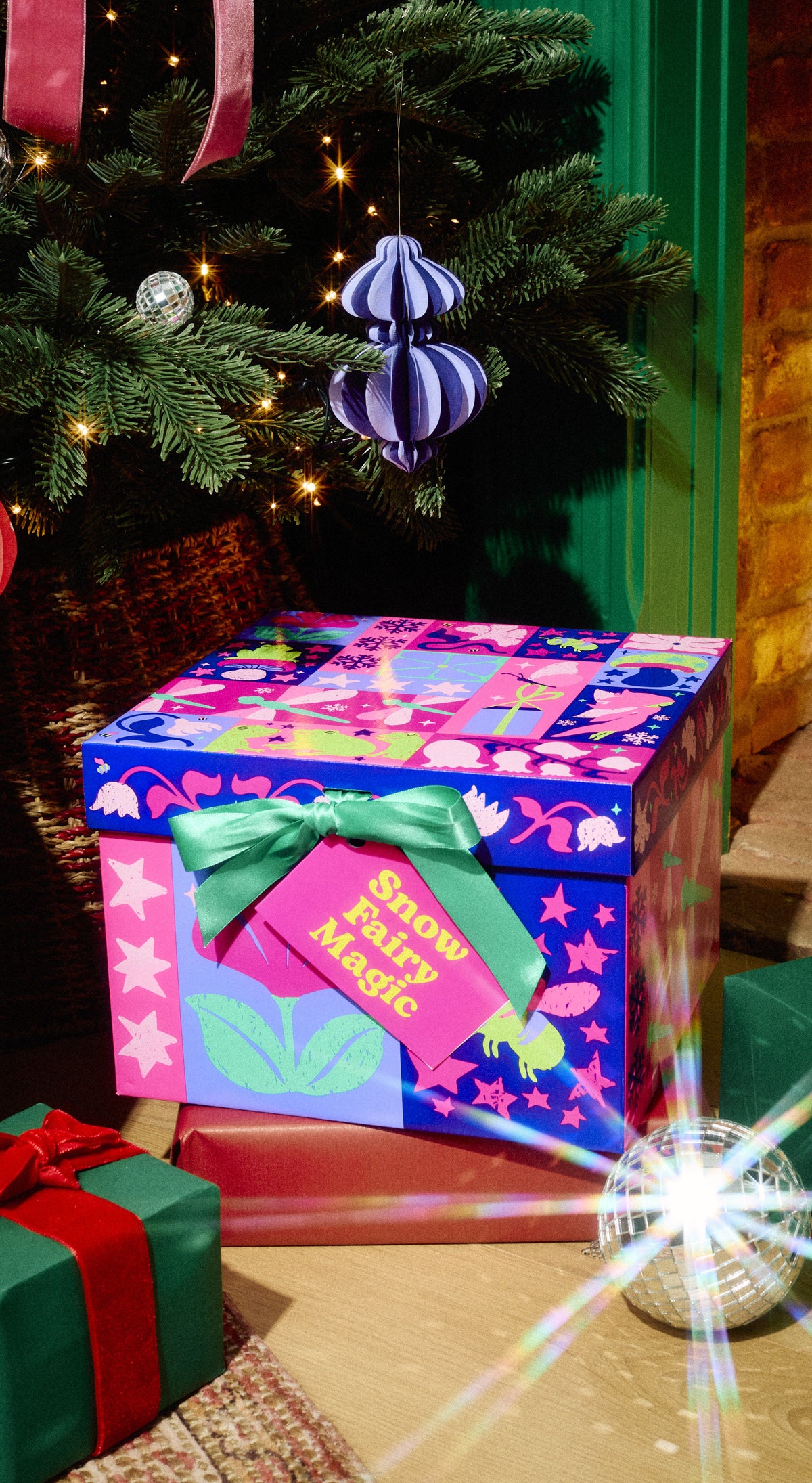 Snow Fairy Magic gift box in pink-and-blue wrapping with a green bow beneath a Christmas tree.