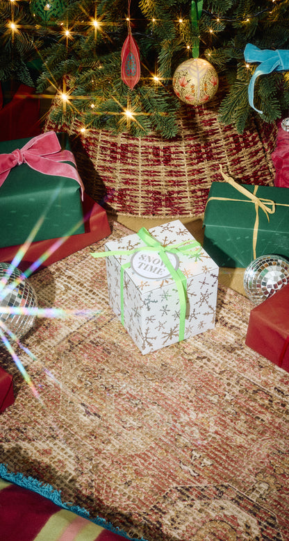 Snow Time gift in pale green-and-white wrapping with a green ribbon beneath a Christmas tree.
