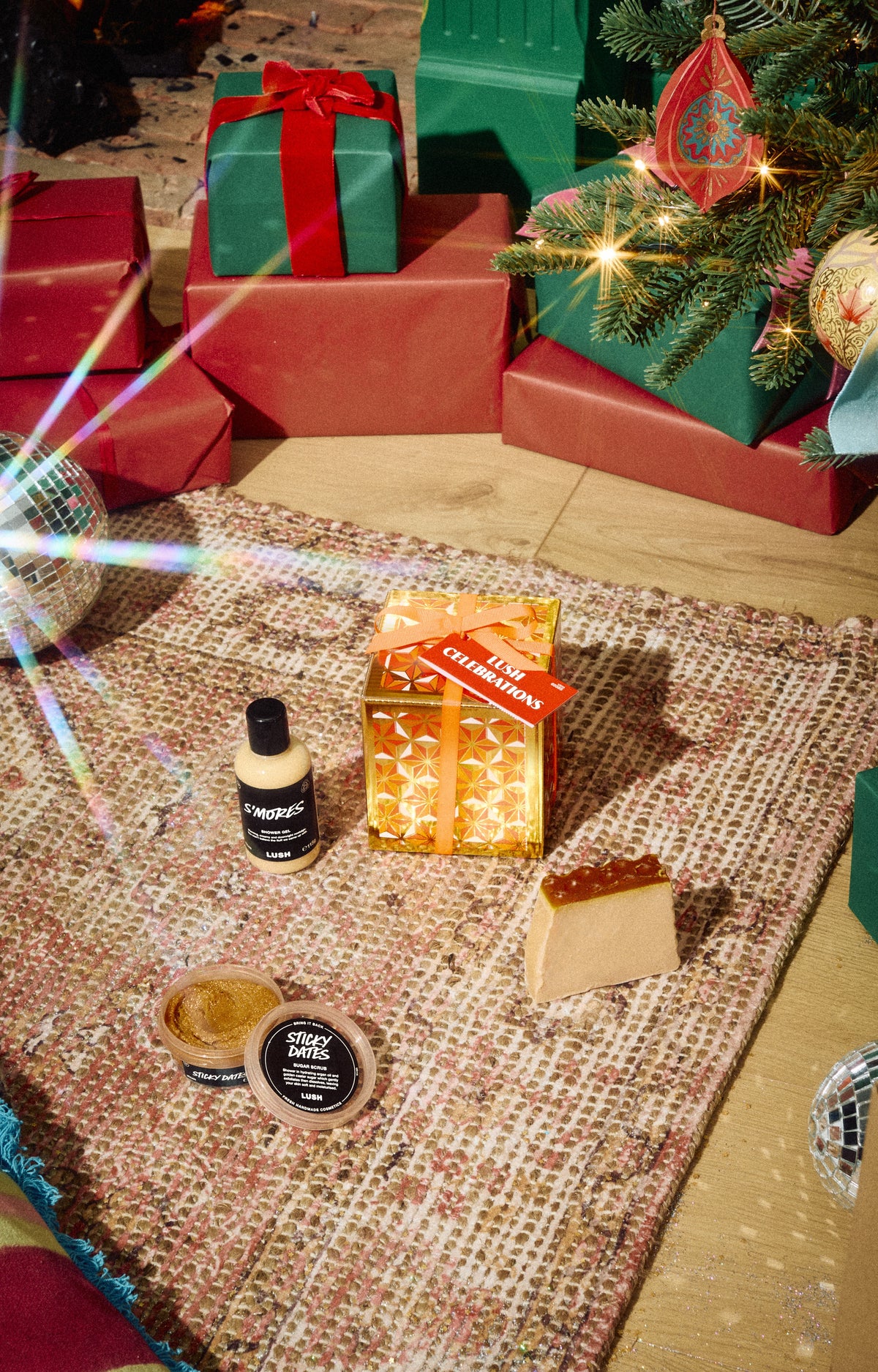 Lush Celebrations gold gift box displayed with a bottle, open pot and pale solid product on a rug.