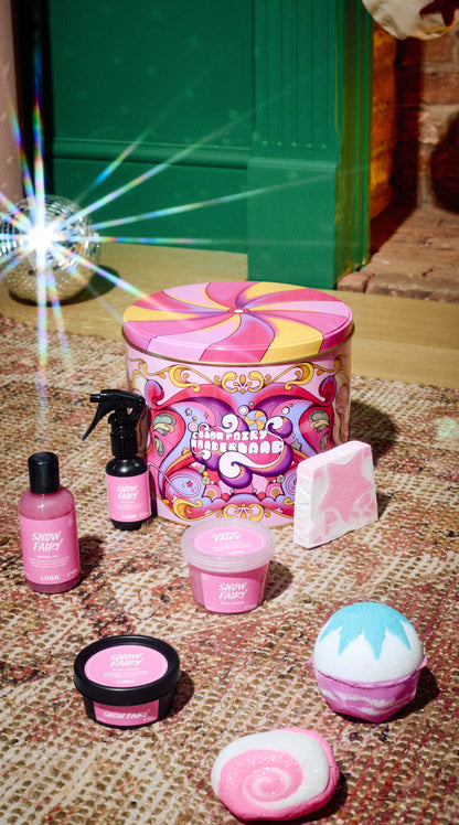 Snow Fairy Wonderland gift tin displayed with pink bath and body products beside a fireplace.