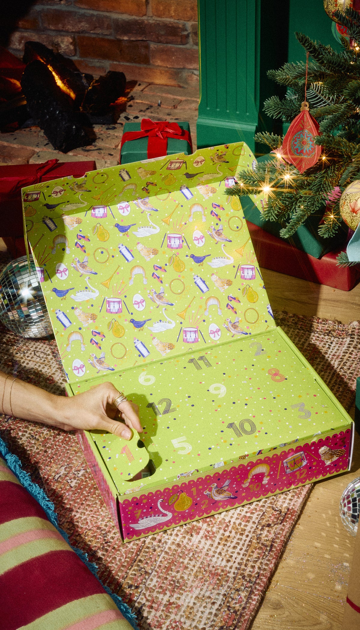 A hand opening the 12 Days of Christmas gift box to reveal its numbered compartments.