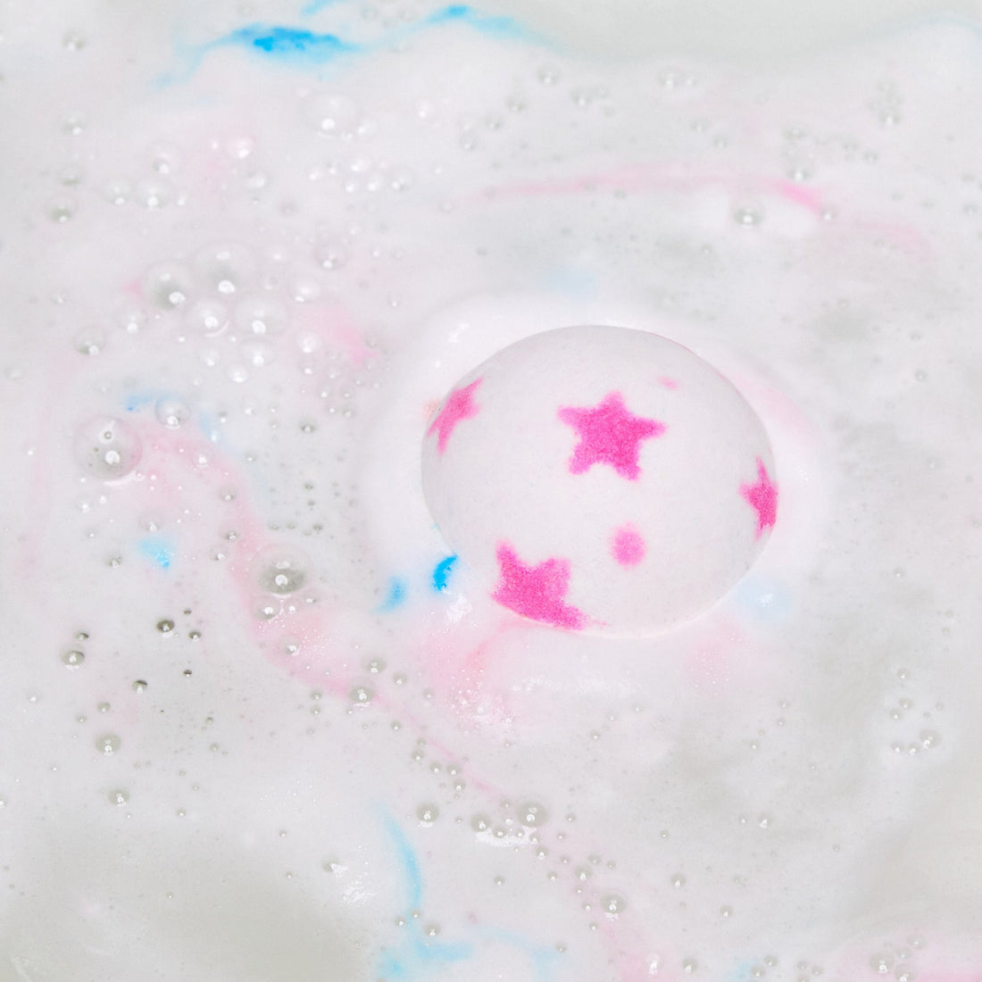 The American Cream bath bomb is slowly dissolving in the bath water giving off a pretty pink and white rippled foam across the surface with a small speck of blue in the centre.