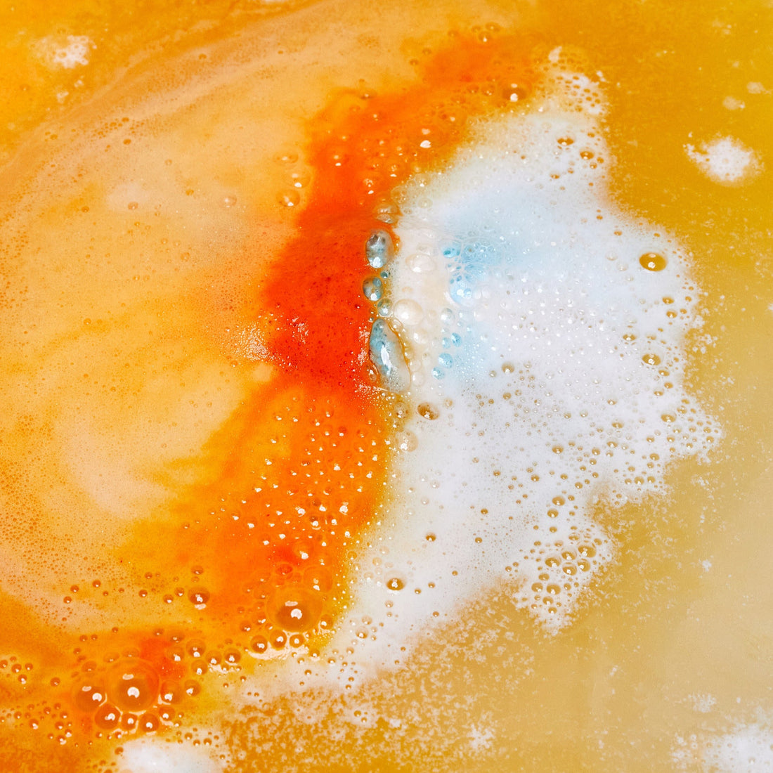 The Chelsea Morning bath bomb is dissolving in the bath water creating layers of foamy, bright orange ripples.