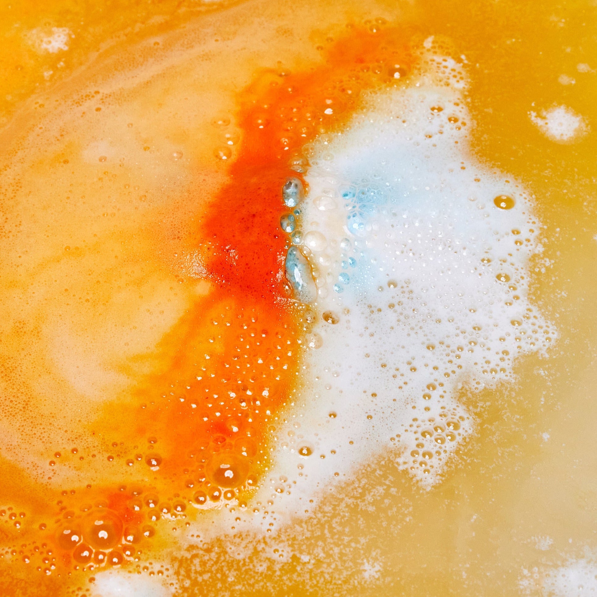 The Chelsea Morning bath bomb is dissolving in the bath water creating layers of foamy, bright orange ripples.