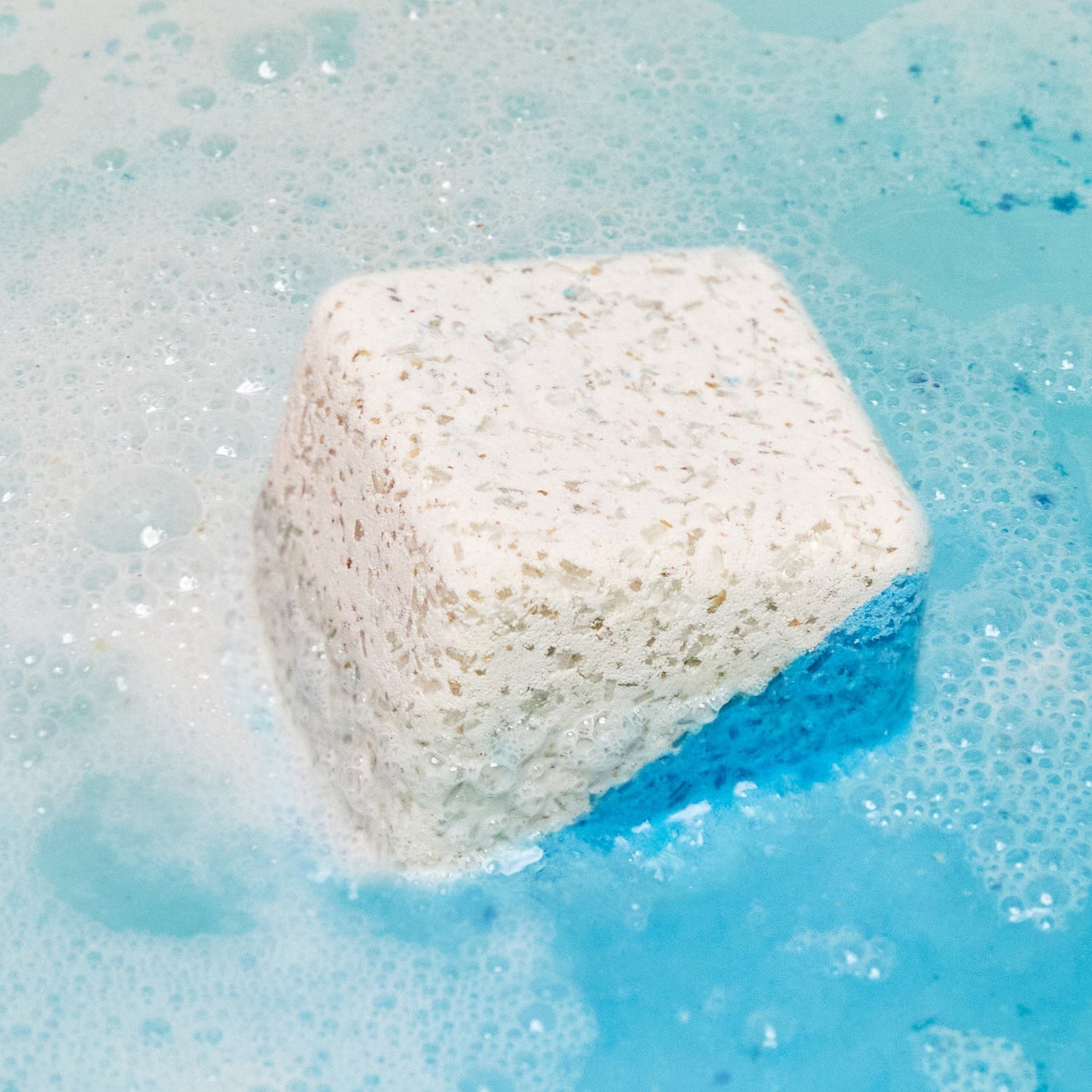 The Dream Cream Epsom salt bath bomb has dissolved leaving clear, turquoise water with a delicate dusting of foam on the surface.