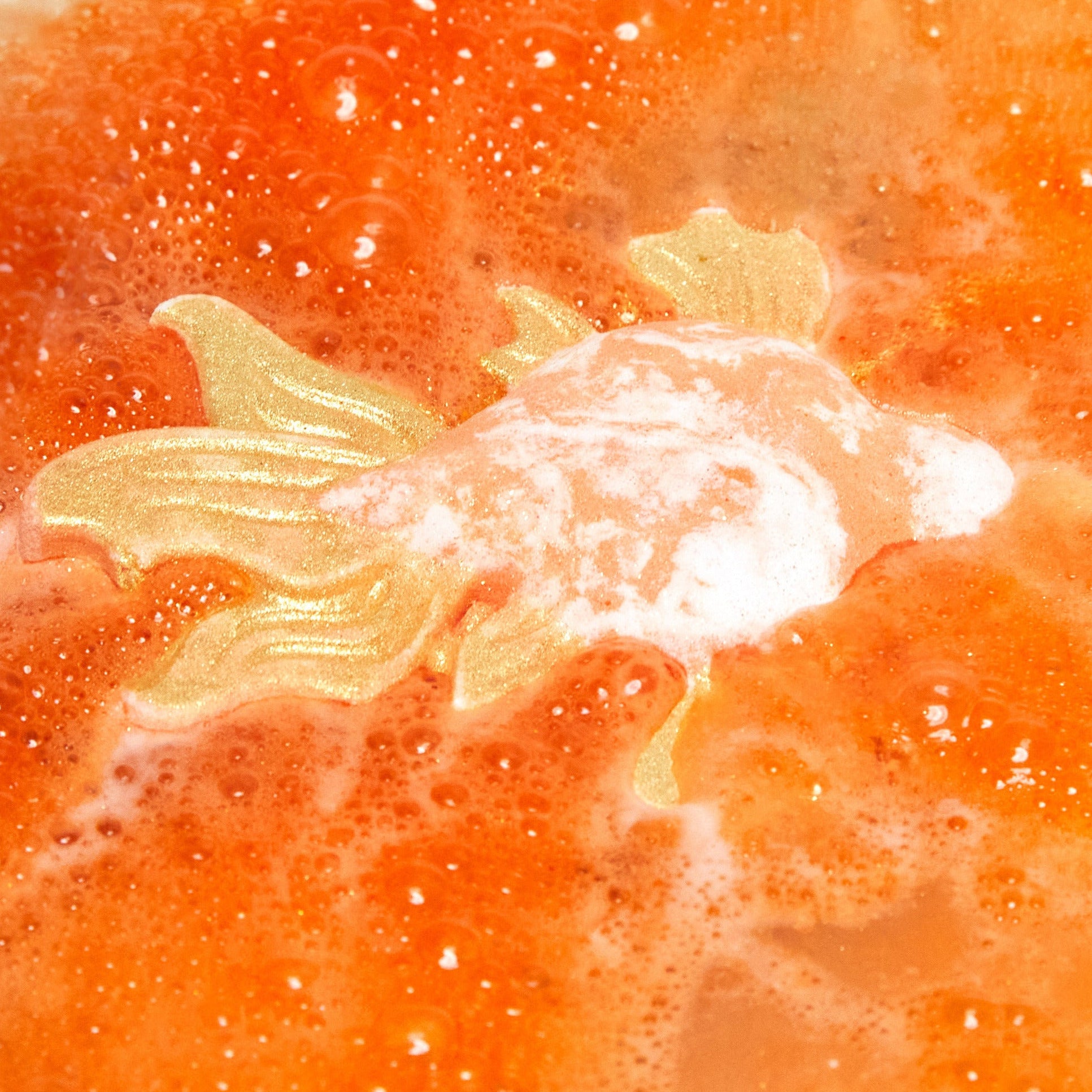 The Goldfish bath bomb is slowly dissolving creating a sea of deep, sunset-orange water and thick, vibrant foam.