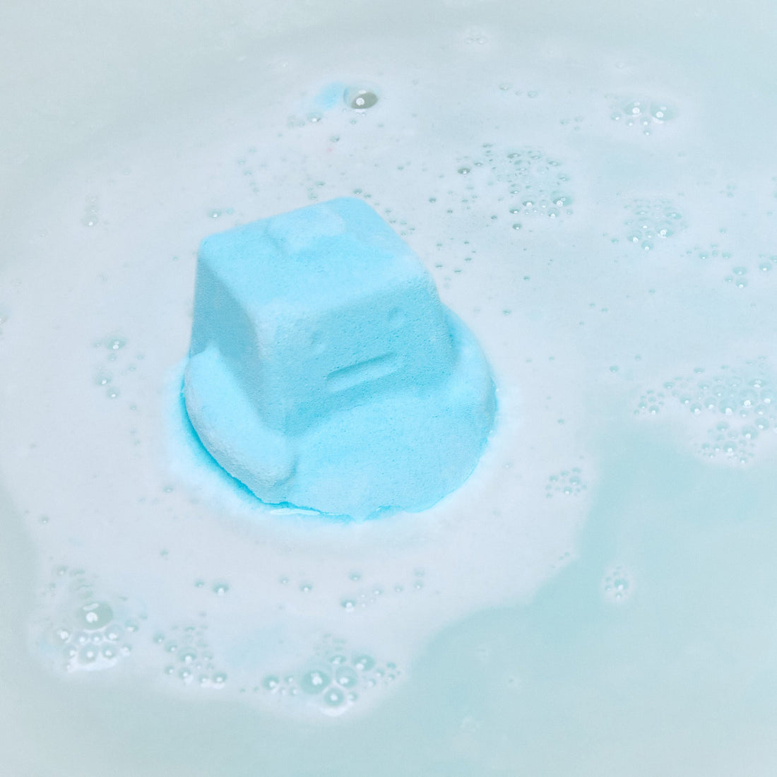 The Ickle Baby Bot bath bomb has completely dissolved in the water leaving behind a surprise mini reusable shampoo bar help by the model above sky blue waters.