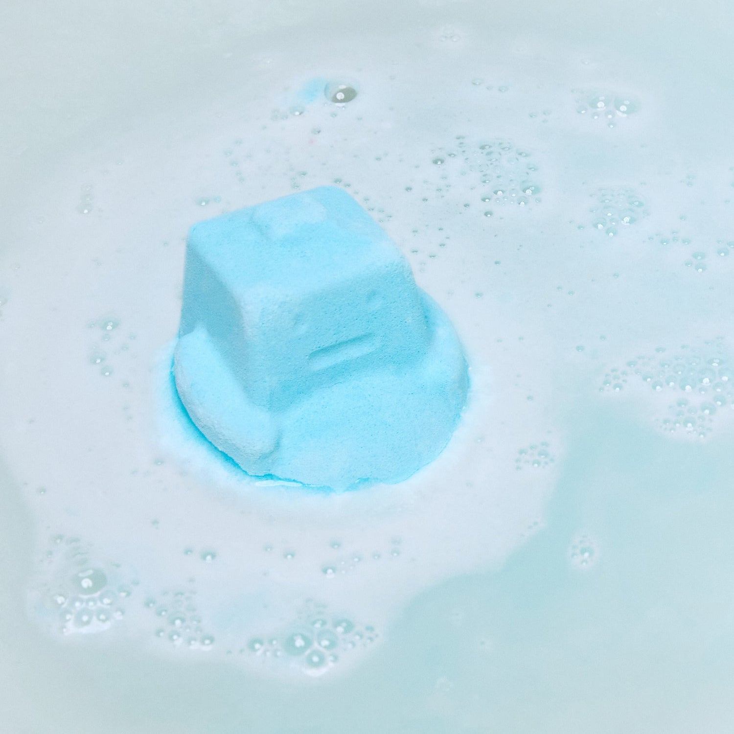 The Ickle Baby Bot bath bomb has completely dissolved in the water leaving behind a surprise mini reusable shampoo bar help by the model above sky blue waters.