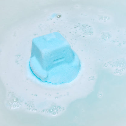 The Ickle Baby Bot bath bomb has completely dissolved in the water leaving behind a surprise mini reusable shampoo bar help by the model above sky blue waters.