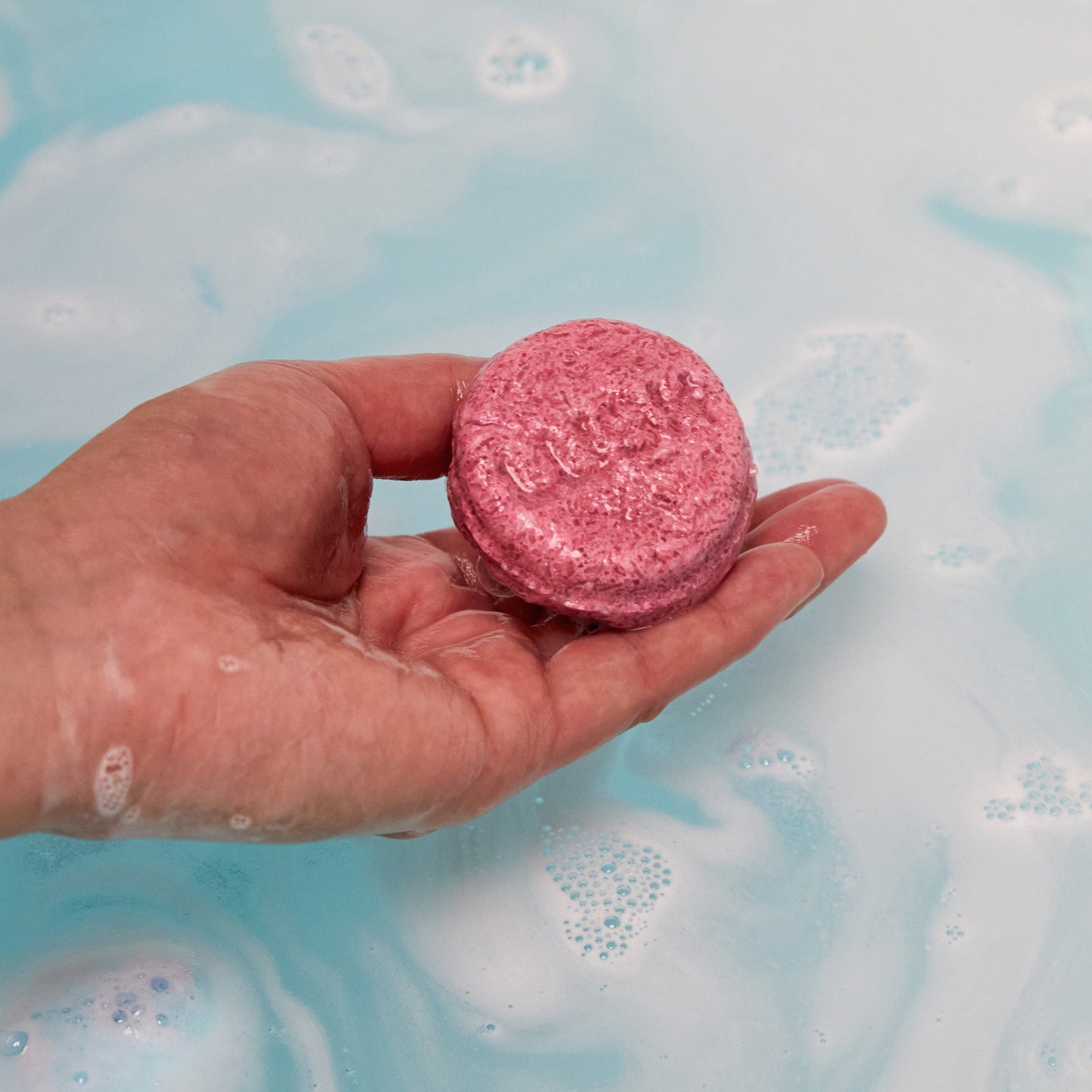 The Ickle Baby Bot bath bomb has completely dissolved in the water leaving behind a surprise mini reusable shampoo bar help by the model above sky blue waters.