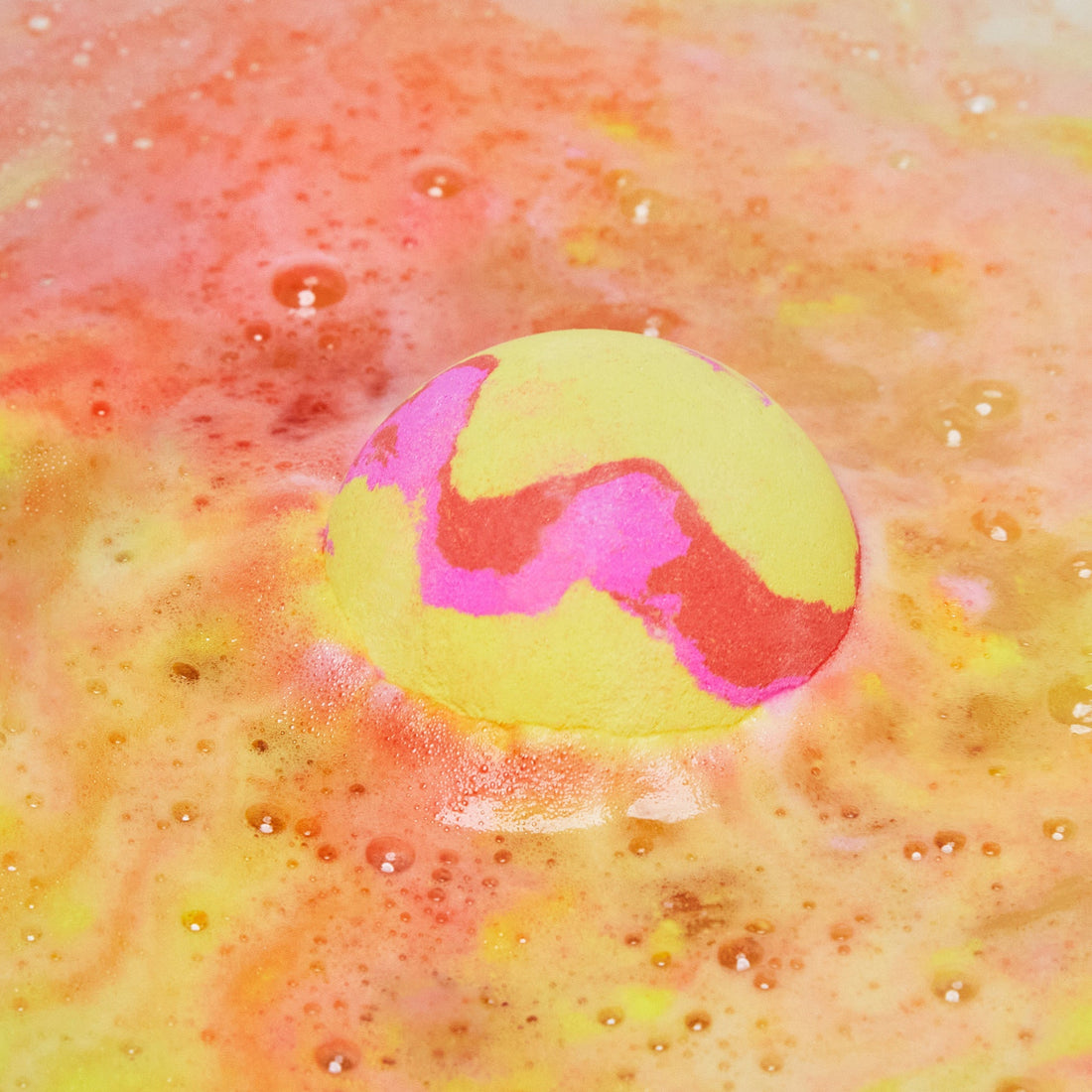 The Passion bath bomb is slowly dissolving creating swirling ripples of yellow, pink and orange.