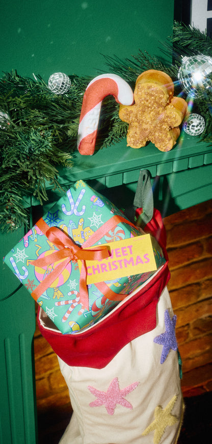 Sweet Christmas gift tucked into a stocking, with candy-cane and gingerbread-shaped products on the mantelpiece.