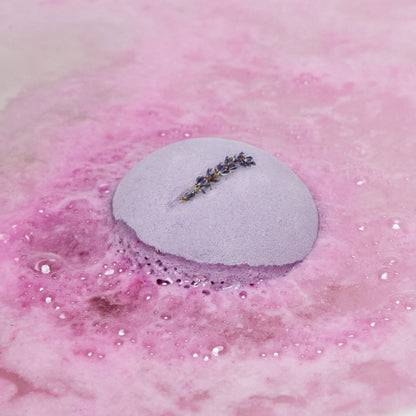 The One With Lavender bath bomb is slowly dissolving in the bath water giving off rippling waves of vivid, hot-pink, velvety foam.