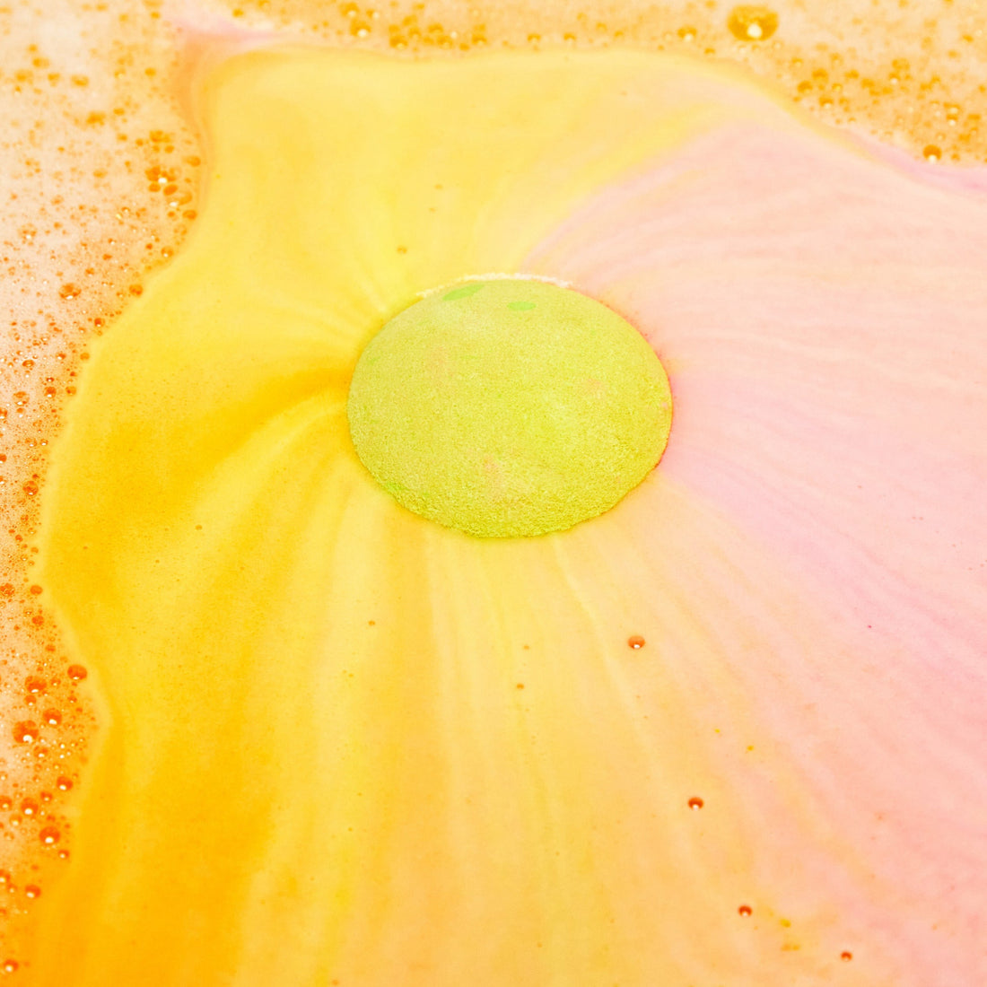 The Time Of The Season bath bomb has been placed into the bath water where it sits like a giant round sun in the centre shooting off swirls of bright yellow and subtle pink like a sunset.