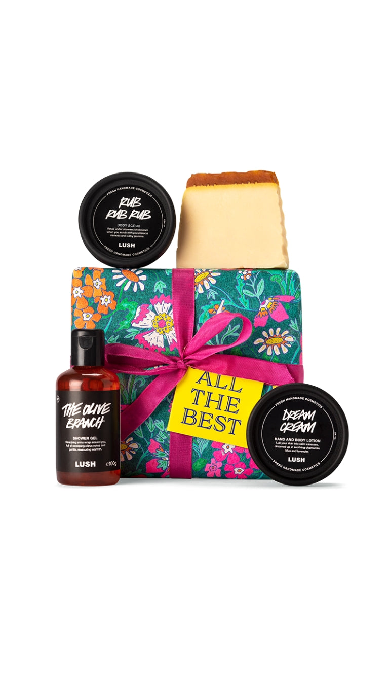 All the Best gift featuring Rub Rub Rub body scrub, Honey I Washed the Kids soap piece, The Olive Branch shower gel and Dream Cream body lotion, displayed around a floral patterned wrapped gift box. 