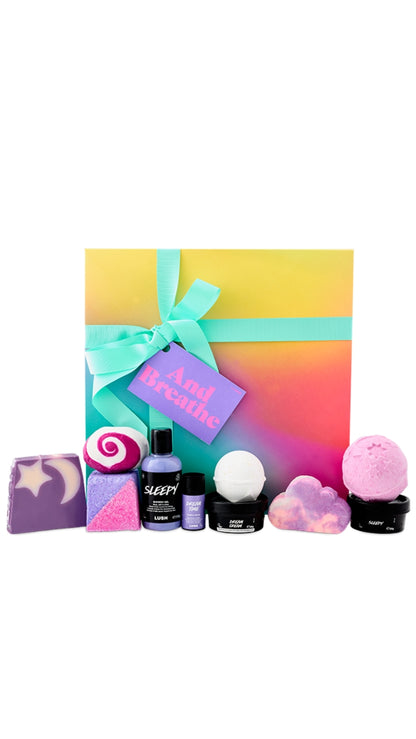 And Breathe Gift featuring a variety of shower, body and bath products displayed in front of a pastel colourful square hat box. 