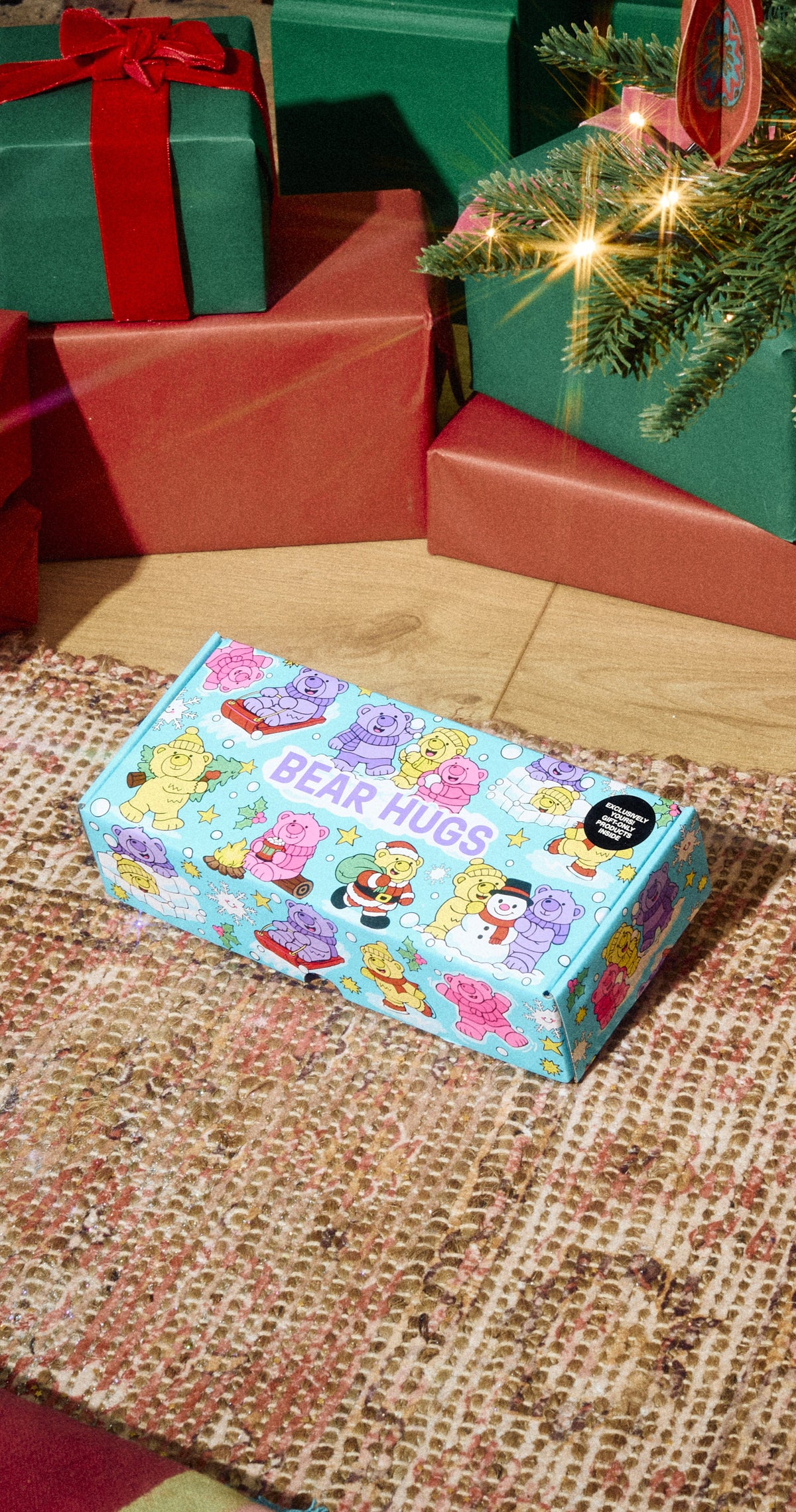 Bear Hugs gift box with colourful bear illustrations on a rug beside Christmas presents.