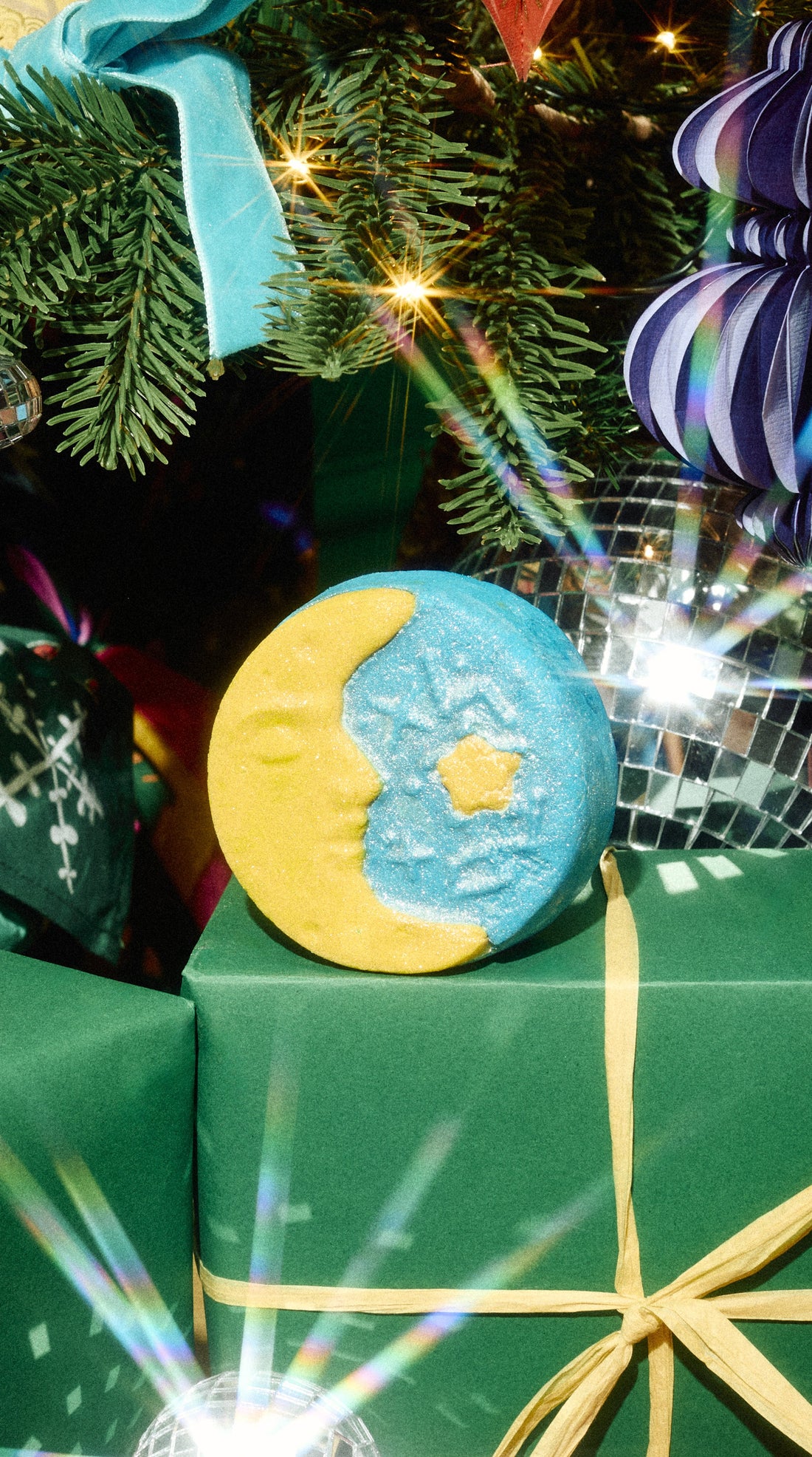 Christmas Eve blue-and-yellow moon-and-star bubble bar resting on a green present beneath a Christmas tree.