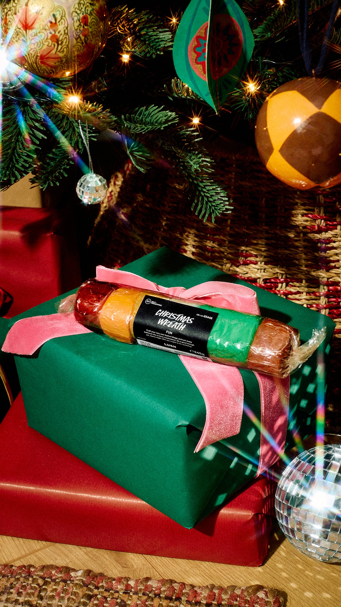 Packaged Christmas Wreath Fun with red, gold and green sections on a present beneath a Christmas tree.