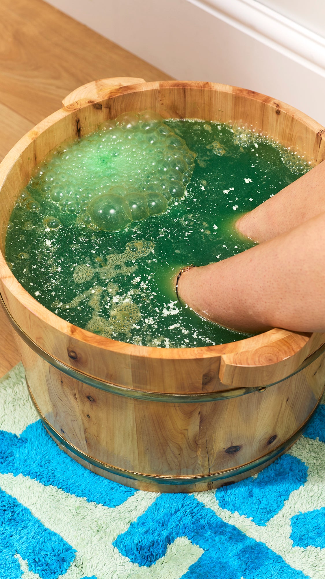 Feet soaking in a wooden bucket of green water, with Dancing Shoes foot soak fizzing near the surface.