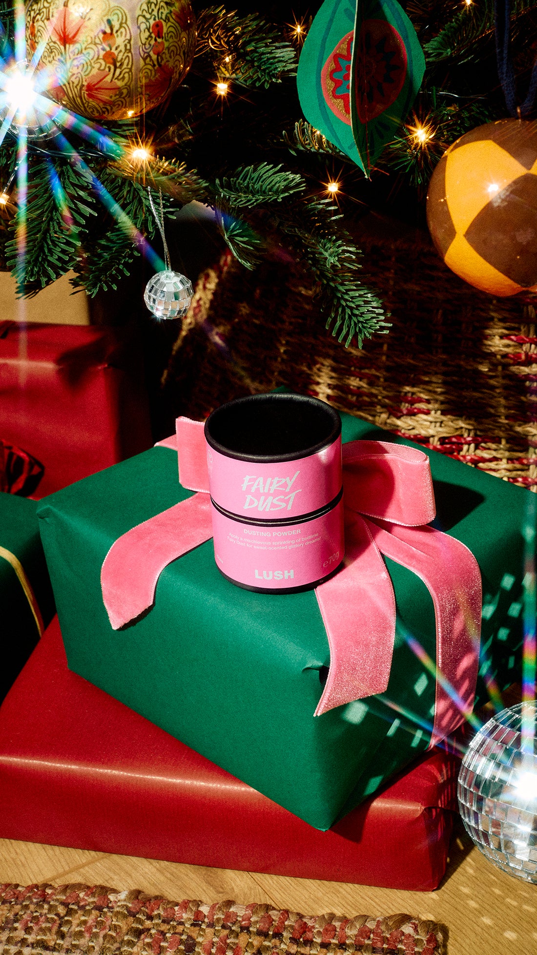Fairy Dust dusting powder resting on a green gift with a pink bow beside a decorated Christmas tree.