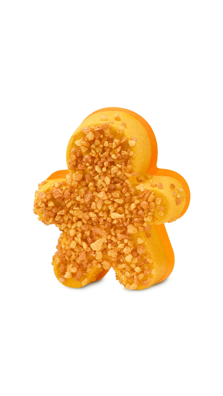 A yellow and orange ginger bread man-shaped bath bomb with loose bits on the top. 
