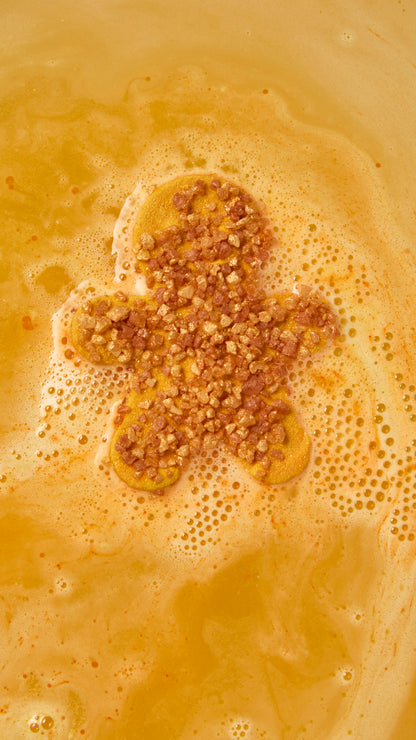 Gingerbread-shaped bath bomb fizzing in golden-orange water with sparkling foam.