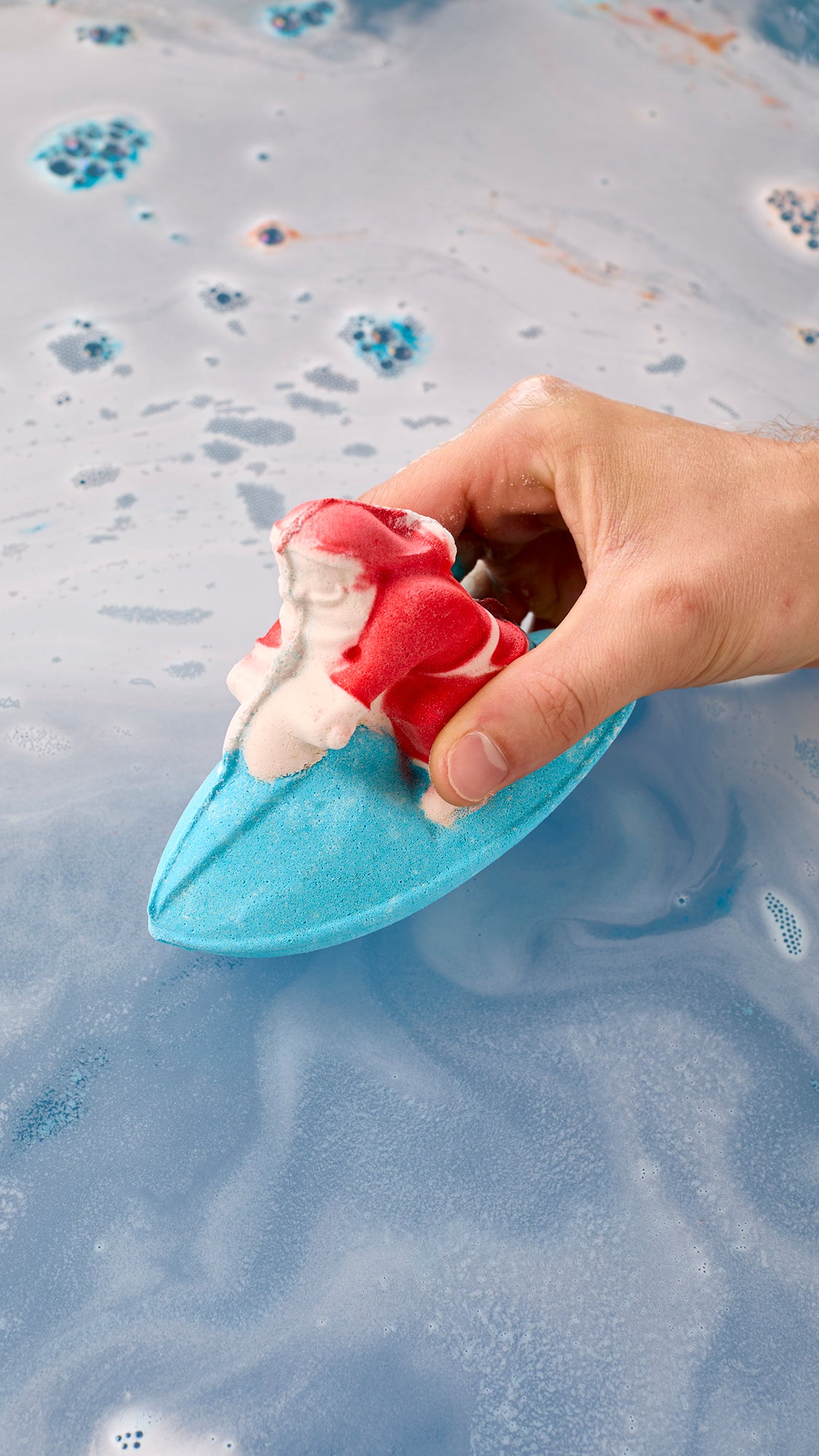 Hand lowering the Santa-on-a-jet-ski bath bomb into blue water.