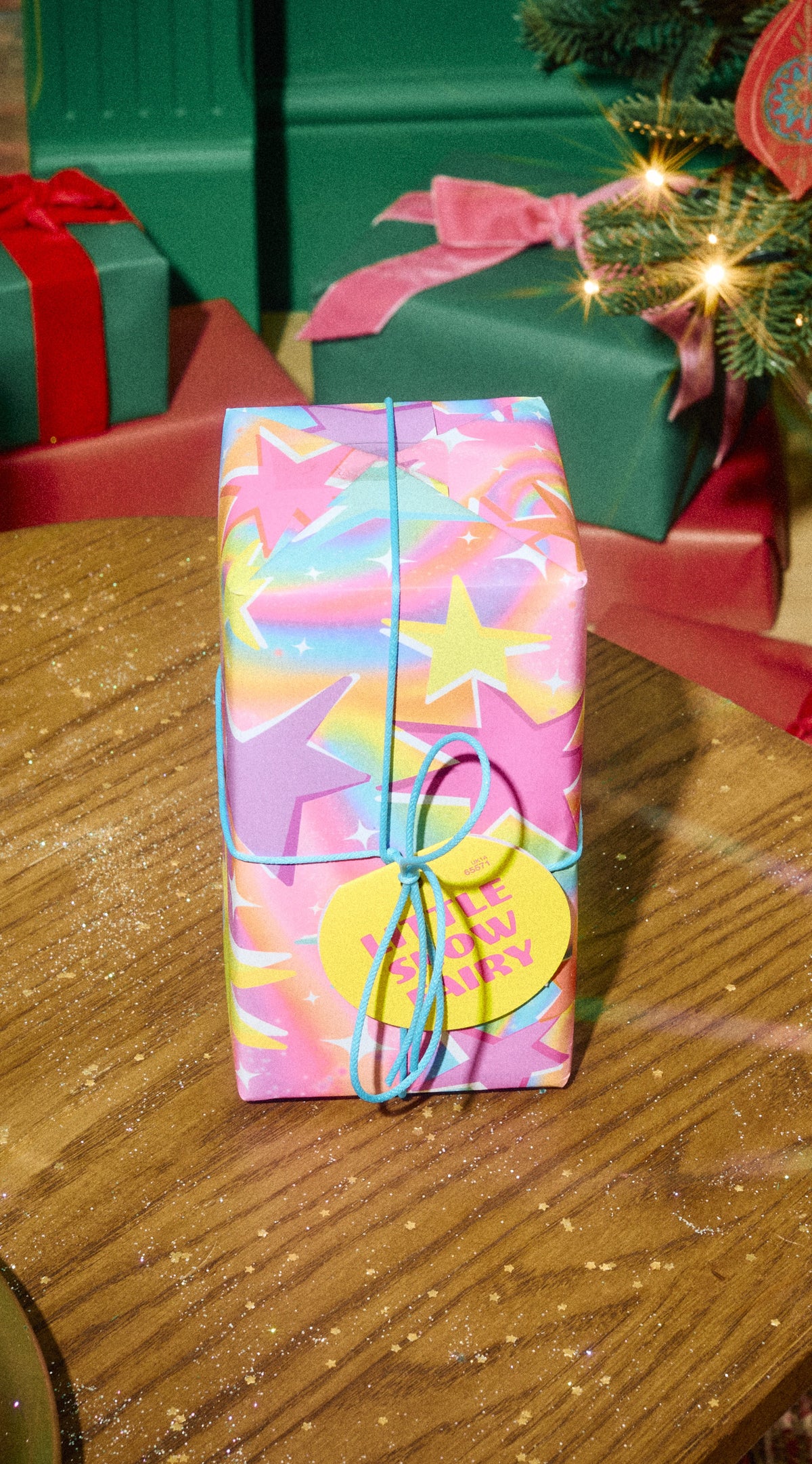 Little Snow Fairy gift in pink and blue star-patterned wrapping with a green ribbon beside Christmas presents.