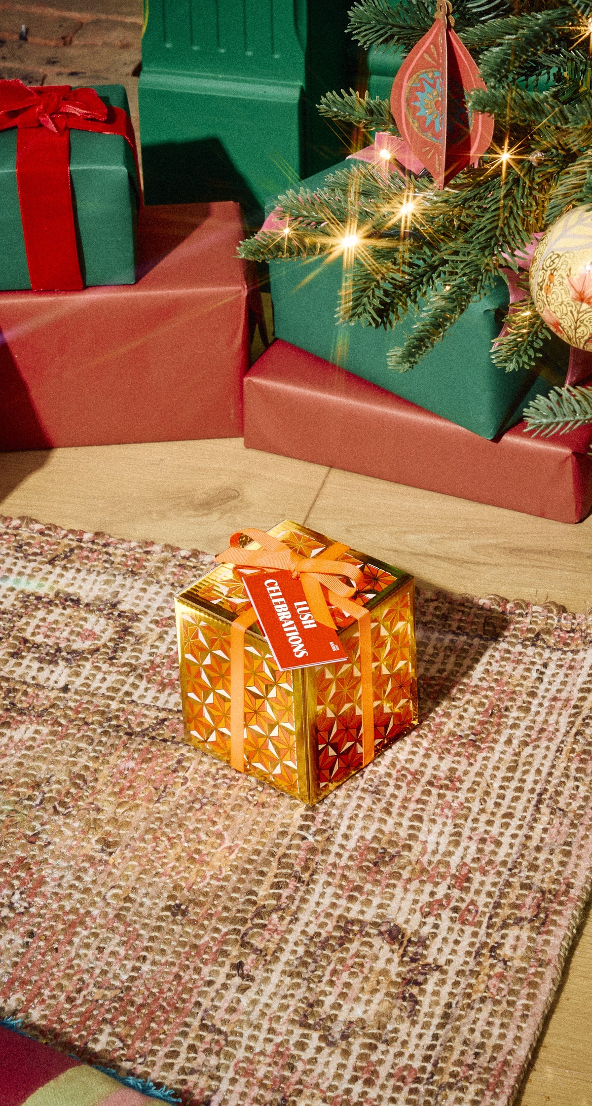 Orange-patterned Lush Celebrations gift box tied with a red ribbon beneath a Christmas tree.