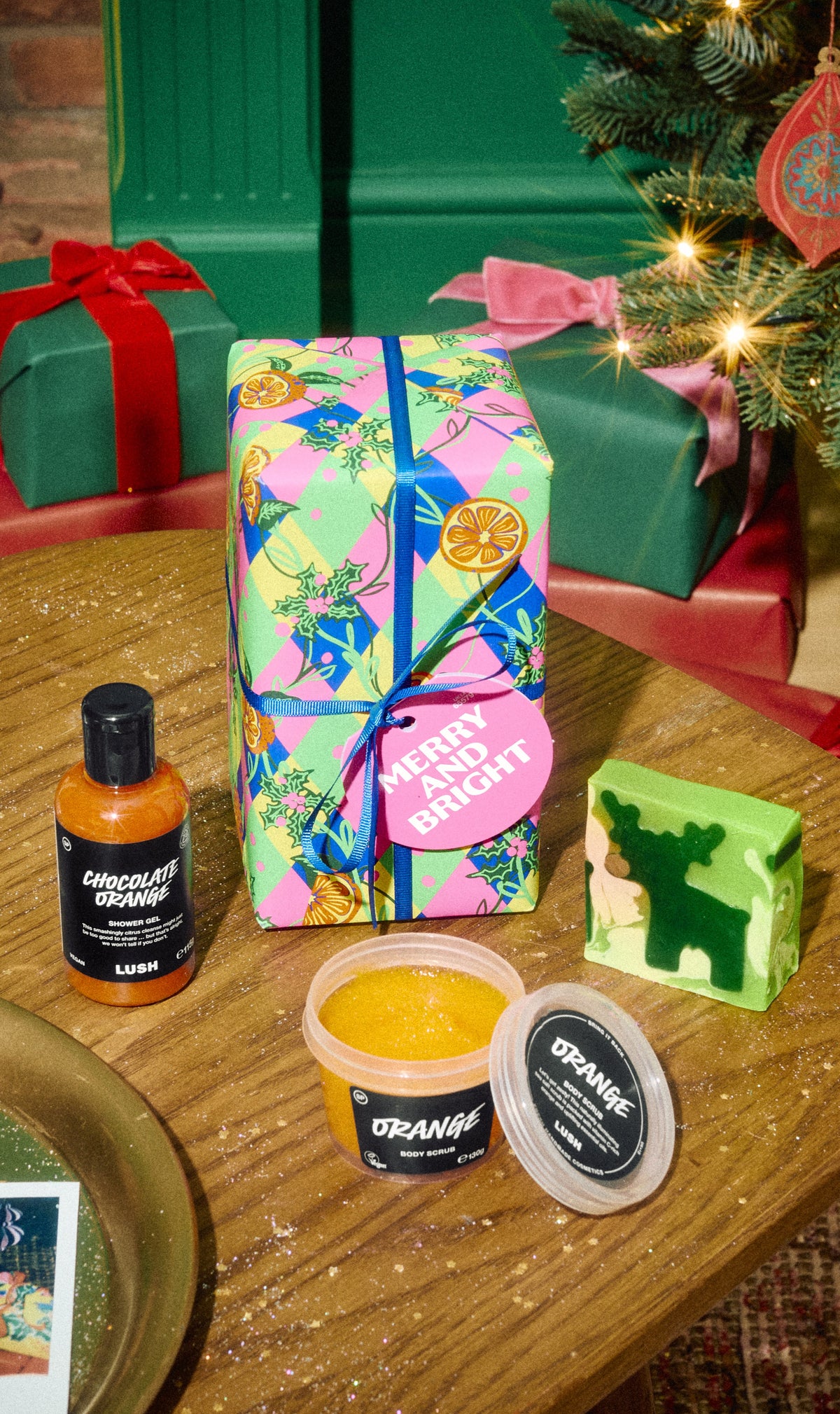 Merry and Bright gift with colourful wrapping, an orange shower gel bottle, an open scrub pot and a green patterned soap.