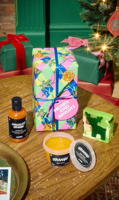 Merry and Bright gift with colourful wrapping, an orange shower gel bottle, an open scrub pot and a green patterned soap.