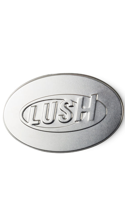 A silver oval-shaped tin with LUSH imprinted on the lid. 