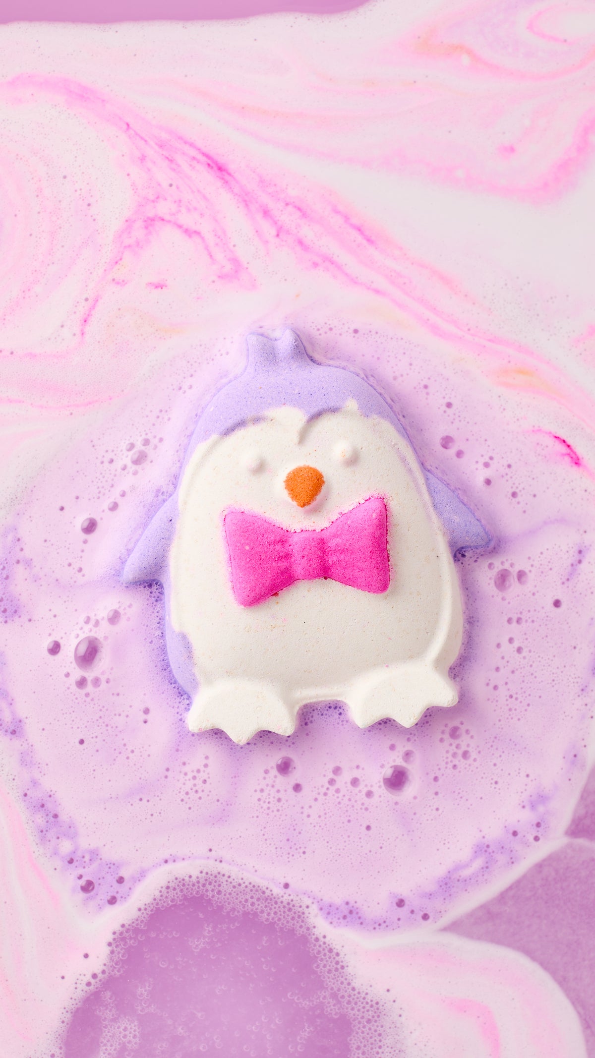 The Christmas Penguin bath bomb fizzing into purple foam in pink and white swirled bathwater.