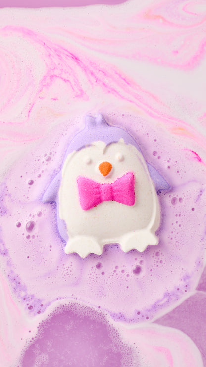 The Christmas Penguin bath bomb fizzing into purple foam in pink and white swirled bathwater.