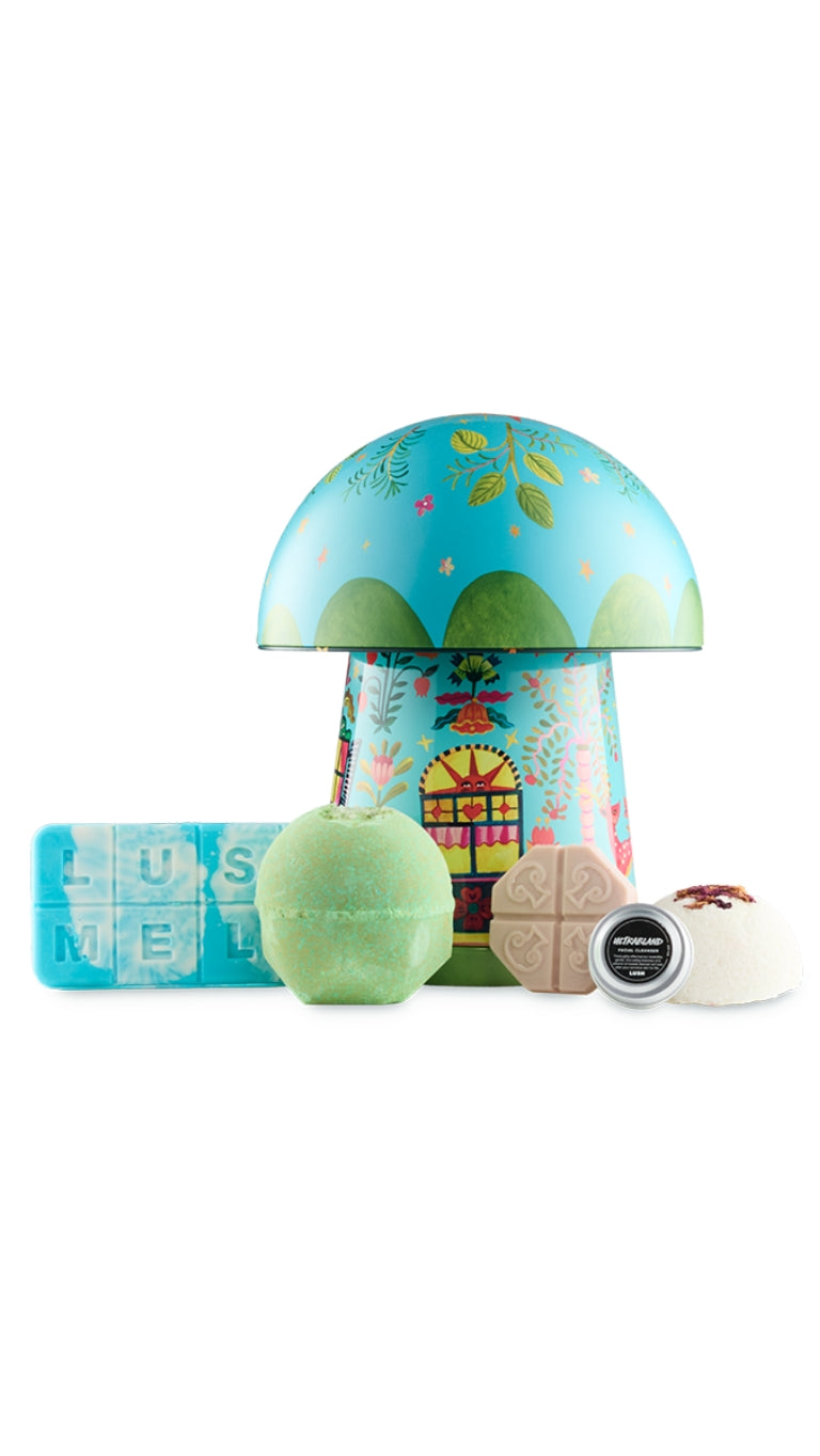 Rewild gift featuring Clear the Air lush melt, Green Fairy bath bomb, Full of Grace facial serum, Ultrabland cleanser, and Comforter Rose solid sugar scrub, displayed in front of a mushroom-shaped gift tin. 