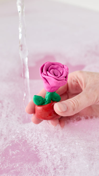 Snow Fairy Fun shaped into a pink rose with green leaves, held above a bubbly bath.