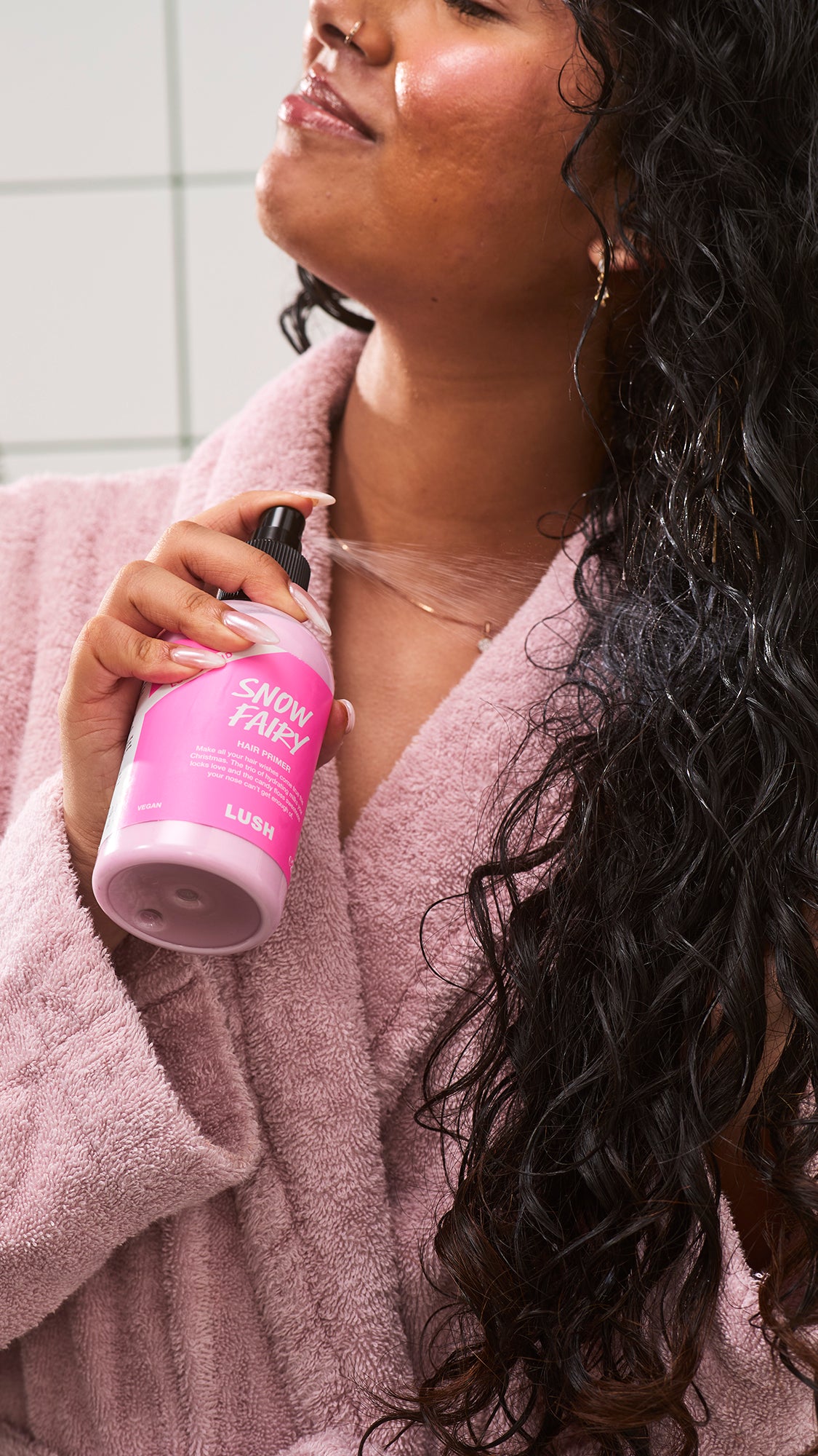 Close-up of a person holding a pink Snow Fairy hair primer bottle beside their curls.