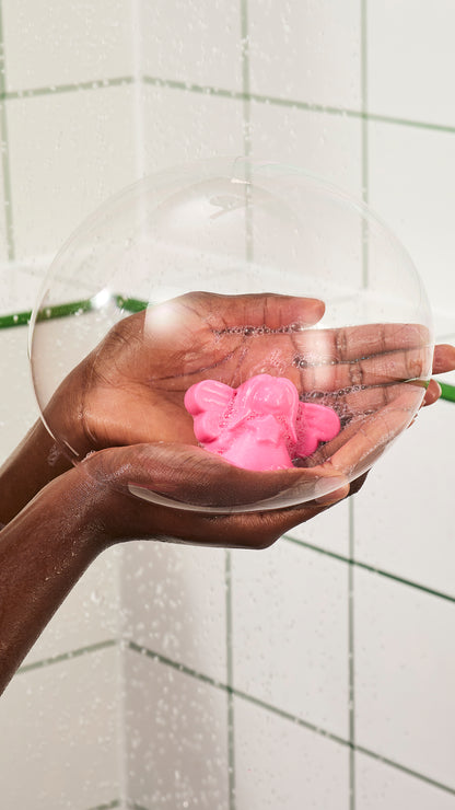 Hands hold pink Snow Fairy shower jelly beneath a large transparent soap bubble.